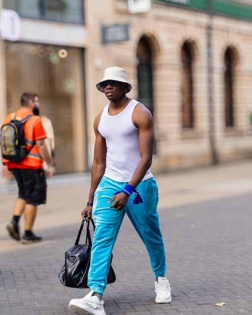 SECKY in a white bucket hat and sky blue trousers crossing a city street