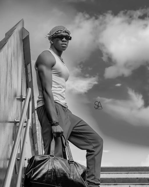Black and white portrait of SECKY on a rooftop staircase against the sky