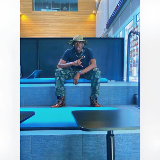 SECKY seated in a bucket hat and camo trousers